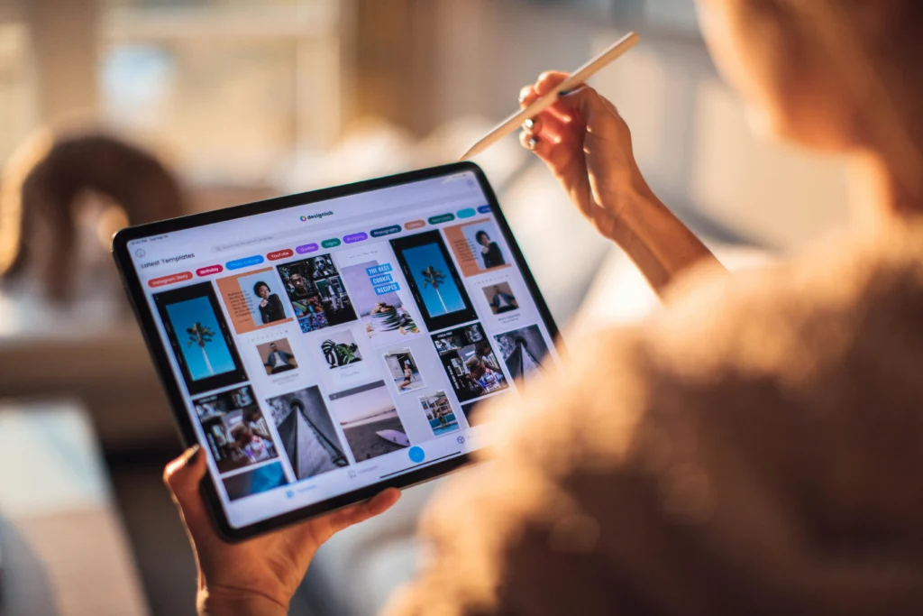 Femme entrain de parcourir des images sur une tablette et elle a un stylet dans la main droite.